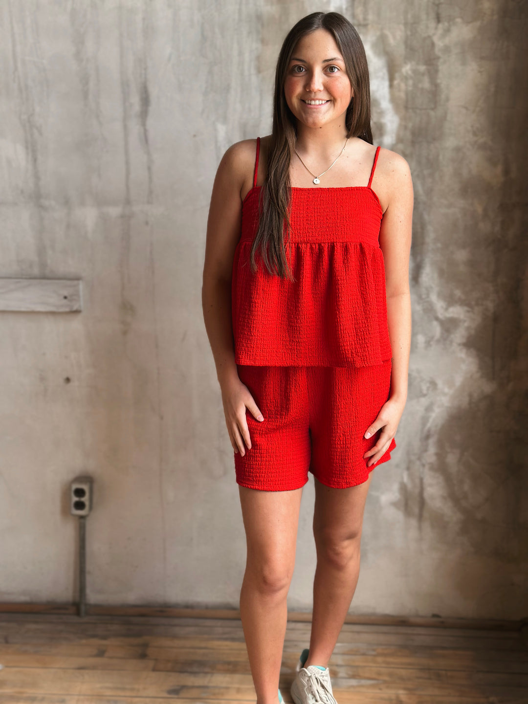 Woman wearing a red outfit standing against a textured wall.