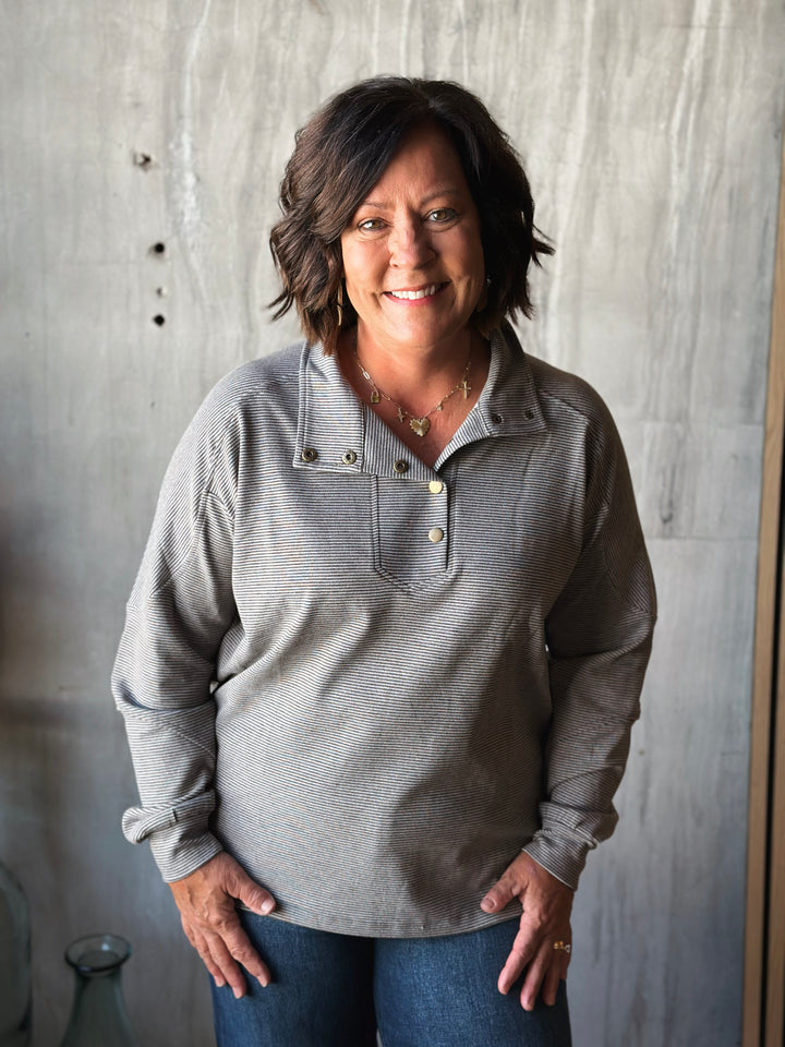 Woman wearing a gray long-sleeve shirt against a textured wall.
