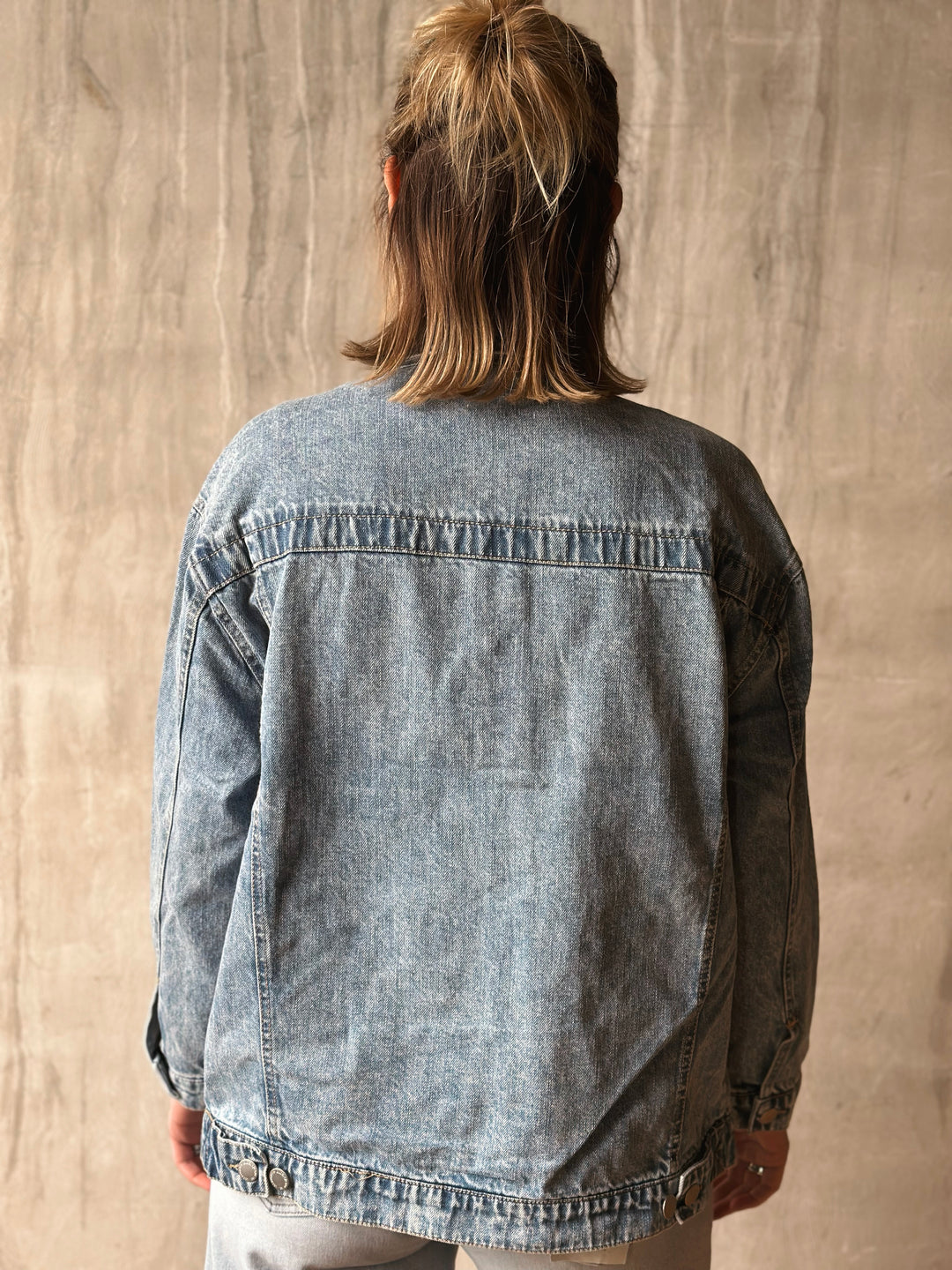 Person wearing a denim jacket against a beige wall