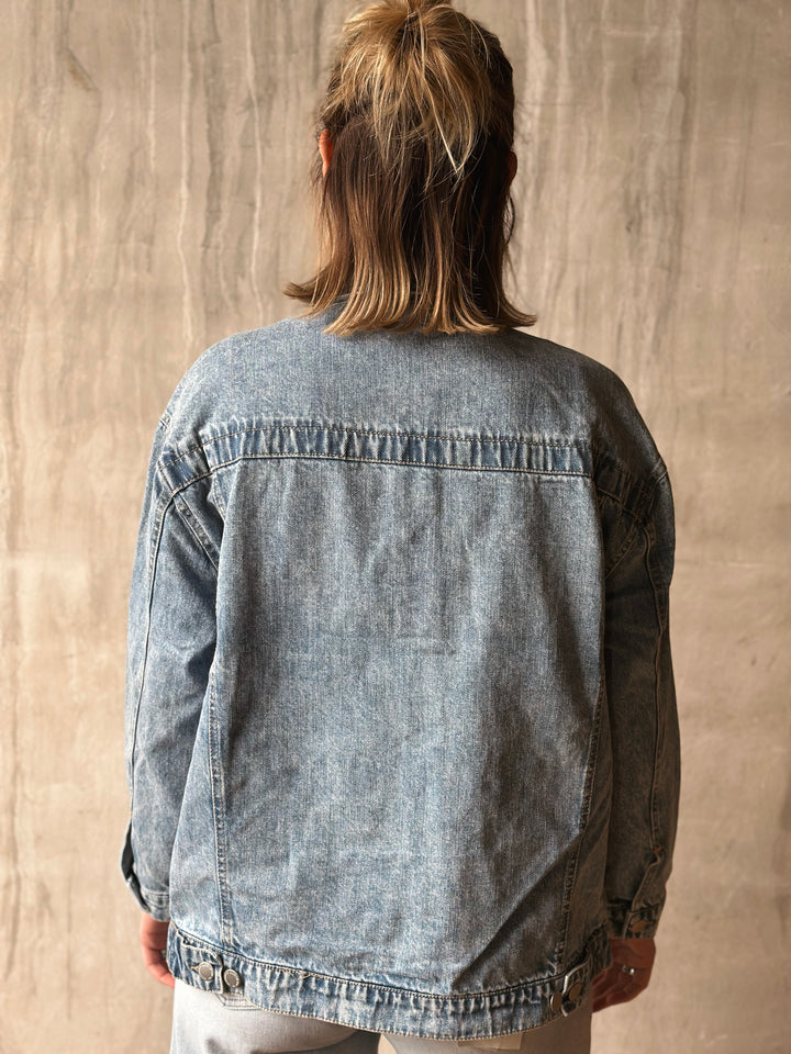 Person wearing a denim jacket against a beige wall