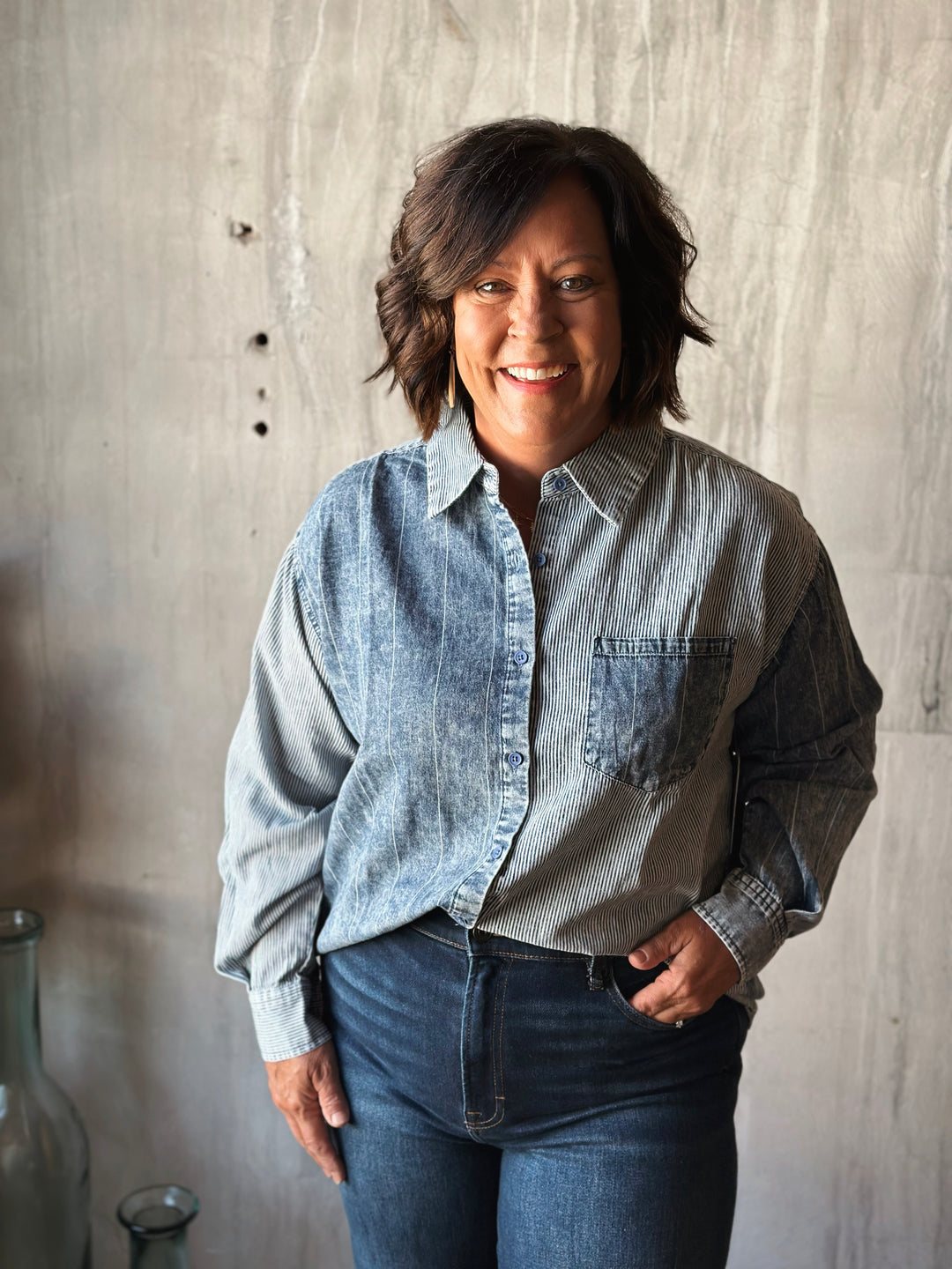 Person wearing a denim shirt with a visible brand logo against a textured wall.