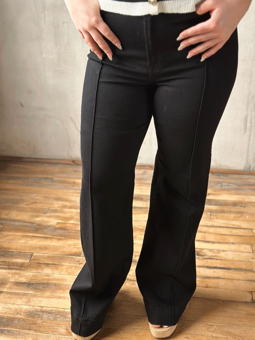 Black jeans worn by a person on a wooden floor with a neutral wall background
