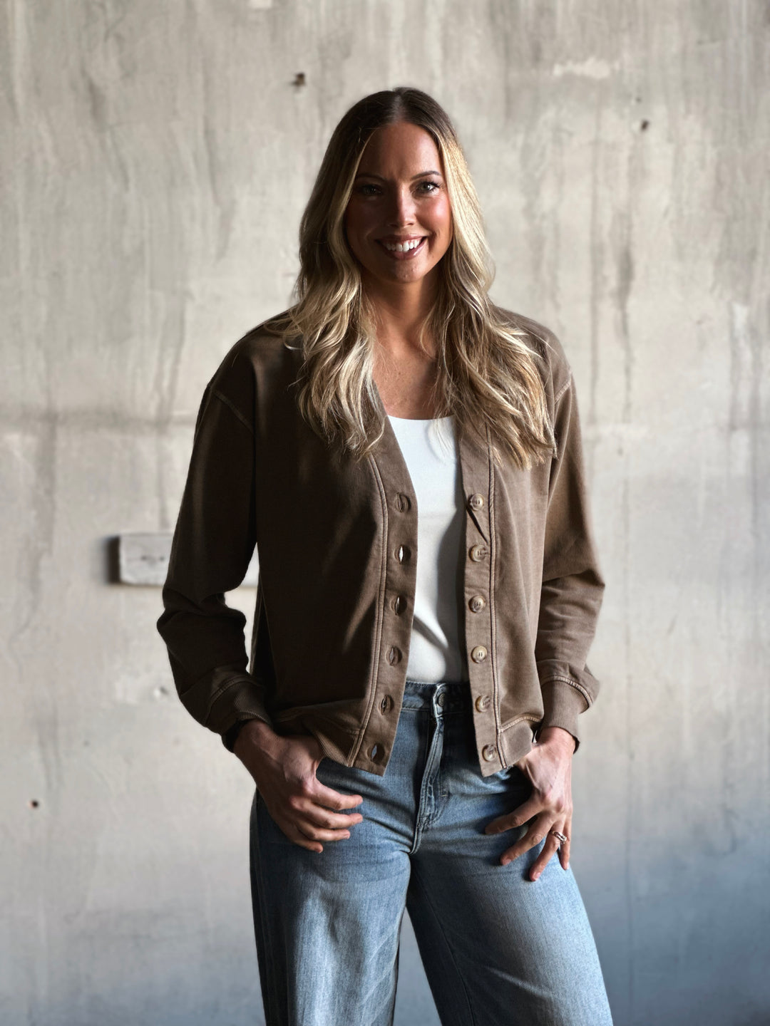 Woman wearing a brown jacket and white shirt against a concrete wall