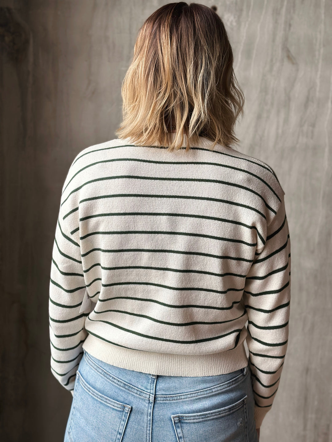 Person wearing a striped sweater and jeans against a neutral background
