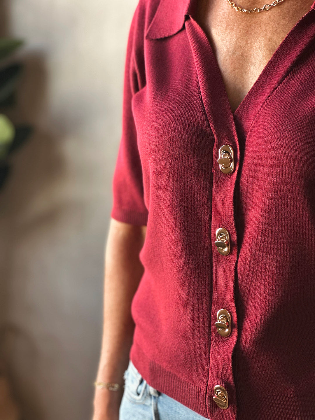 Red cardigan with gold buttons worn by a person, blurred background