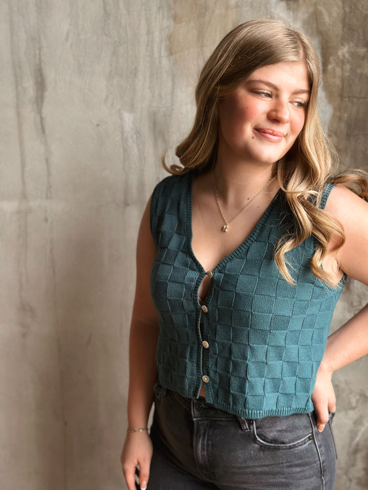 Woman wearing a teal checkered vest against a textured wall