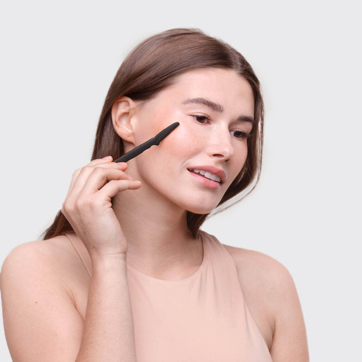 Woman applying makeup with a brush on a plain background
