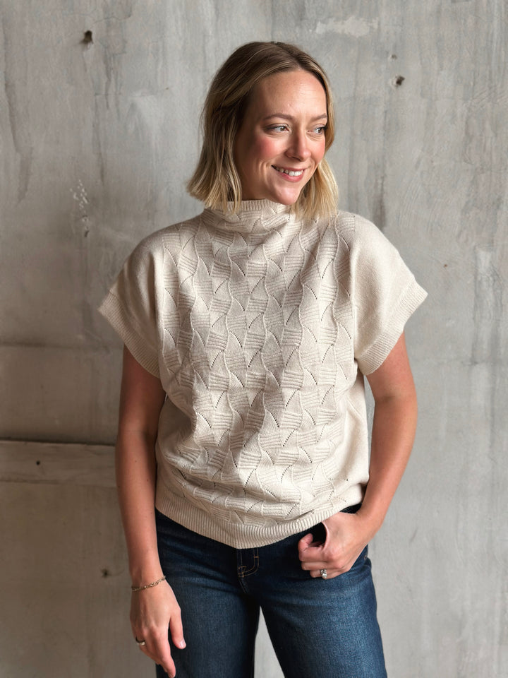 Woman wearing a beige knitted sweater against a gray concrete wall