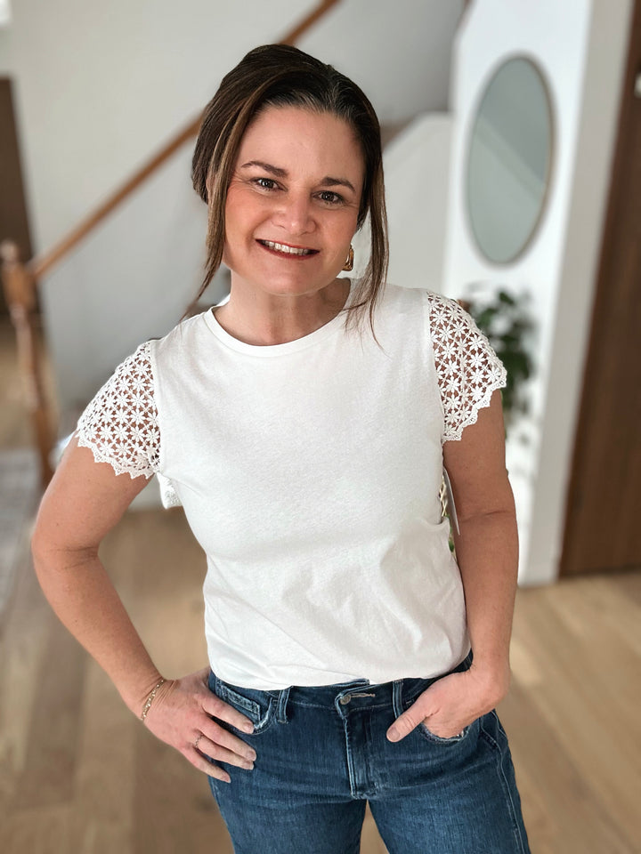 Woman wearing a white t-shirt with lace sleeves and blue jeans indoors.