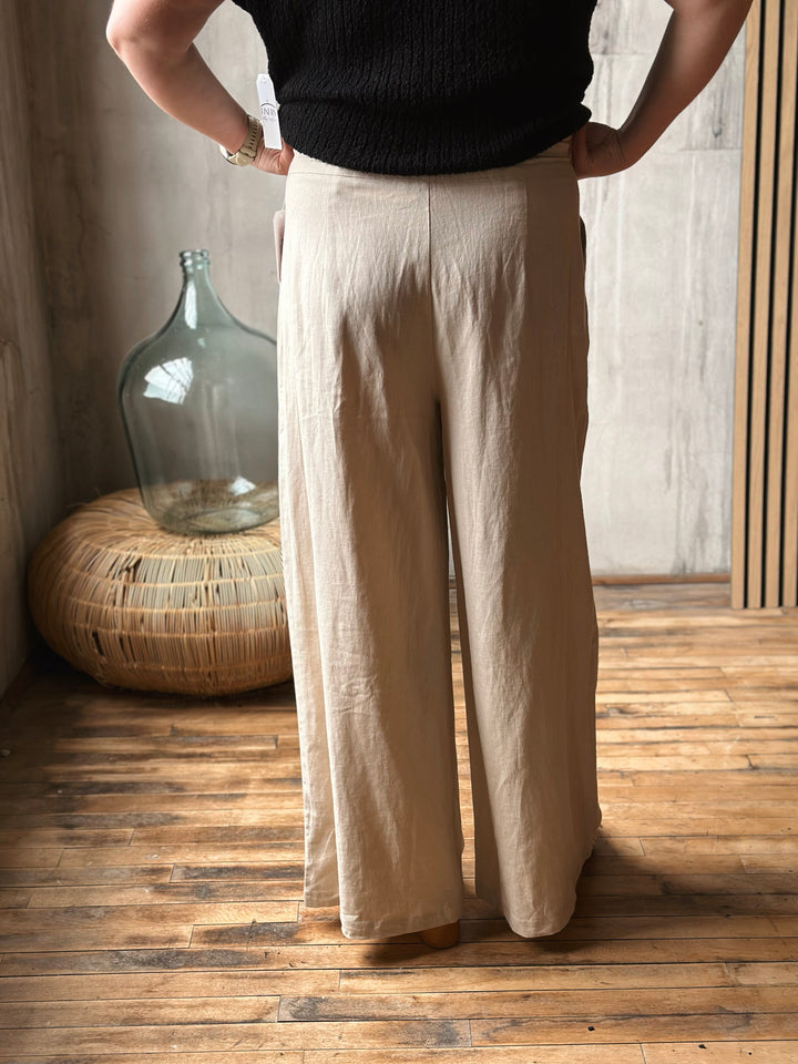 A person wearing beige pants standing in a room with wooden floor and large glass bottle.