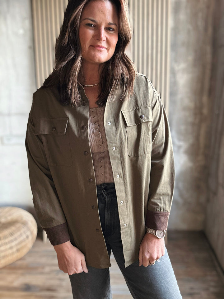 Woman wearing a long olive green shirt with brown cuffs and trim in an indoor setting.