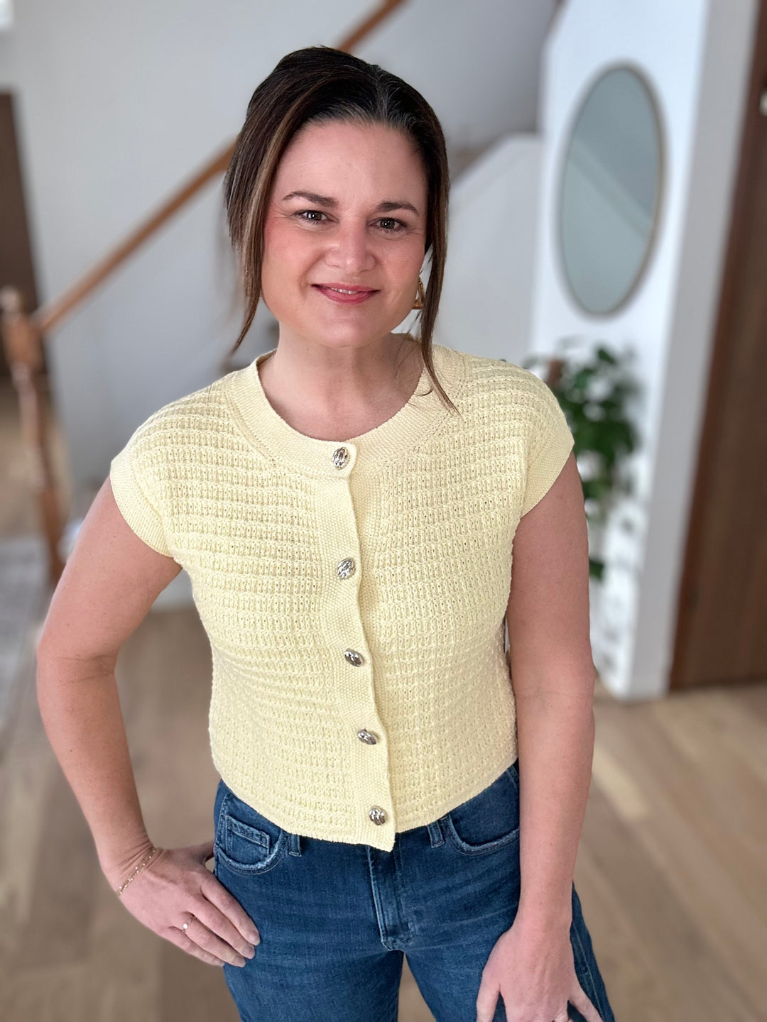 Woman wearing a yellow knitted vest and blue jeans indoors.