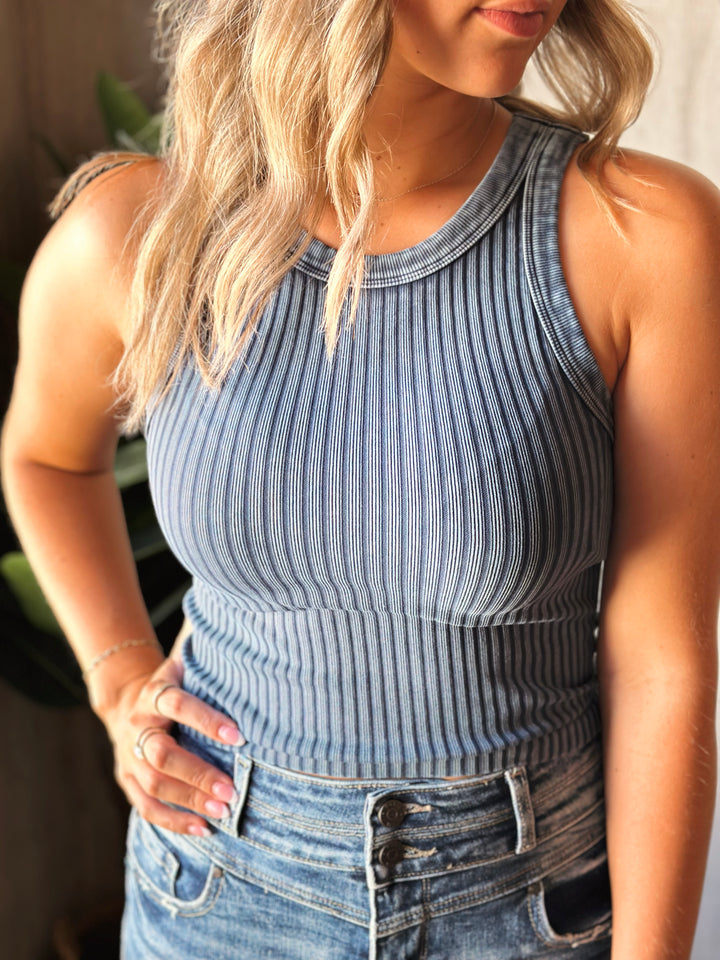 Woman wearing a blue ribbed tank top and jeans with a blurred background