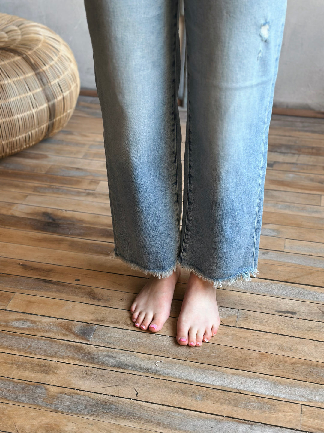 Person wearing light blue jeans standing on a wooden floor.