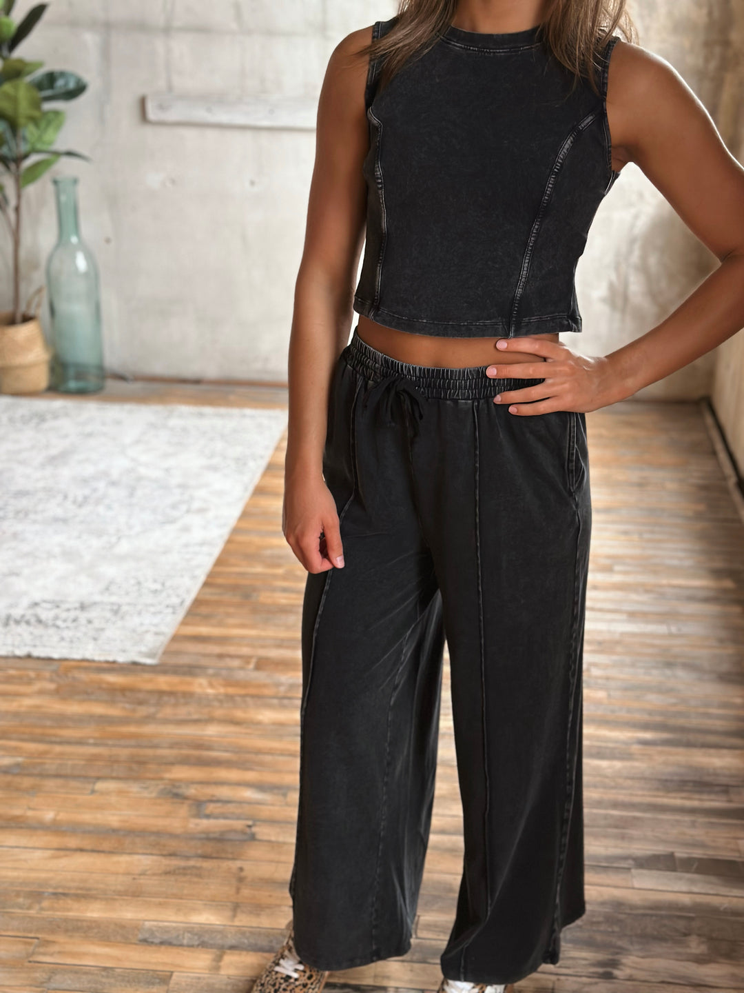 Person wearing a black sleeveless top and wide-leg pants in an indoor setting.
