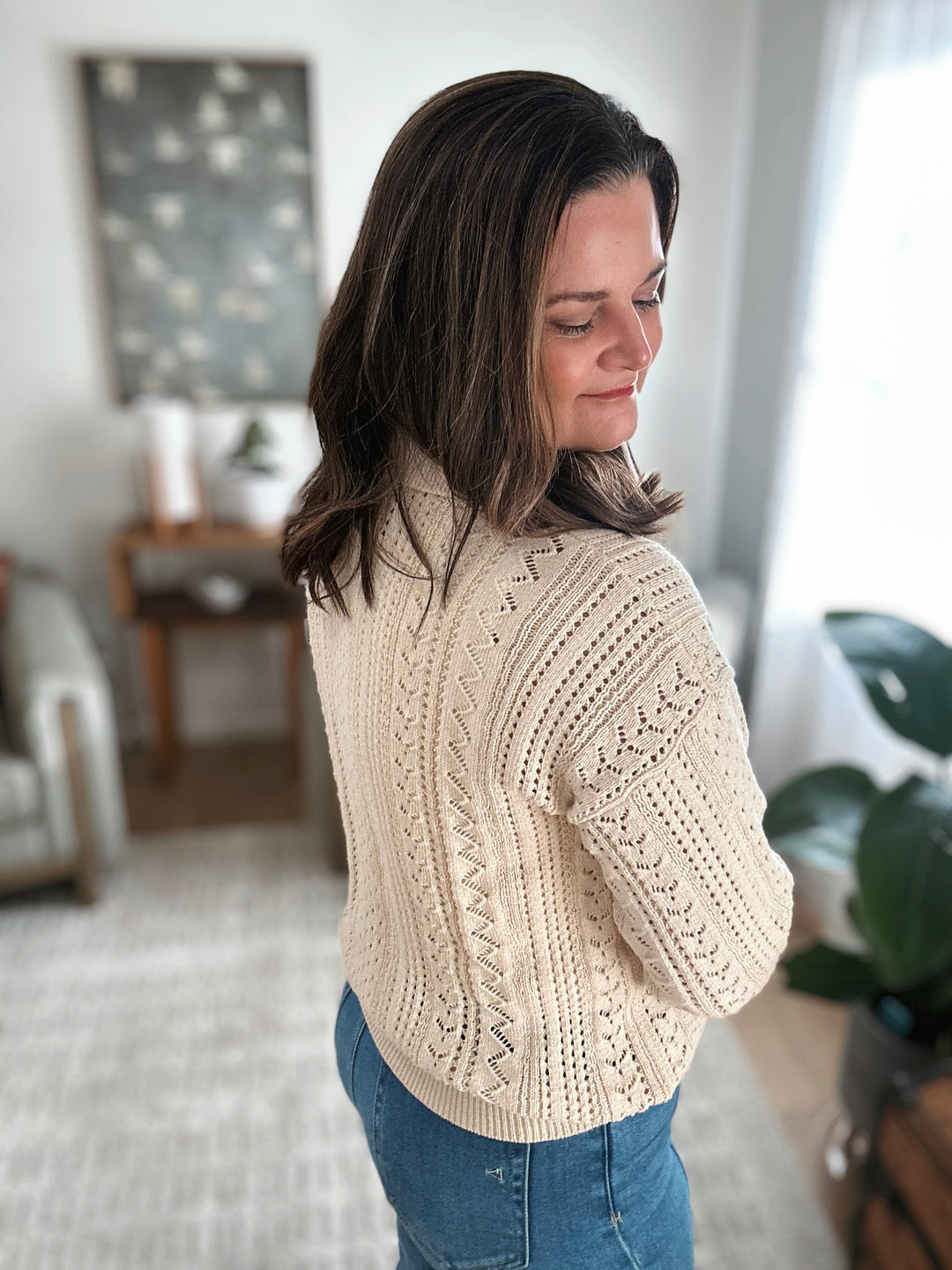 Woman wearing a beige knitted sweater in a cozy living room.
