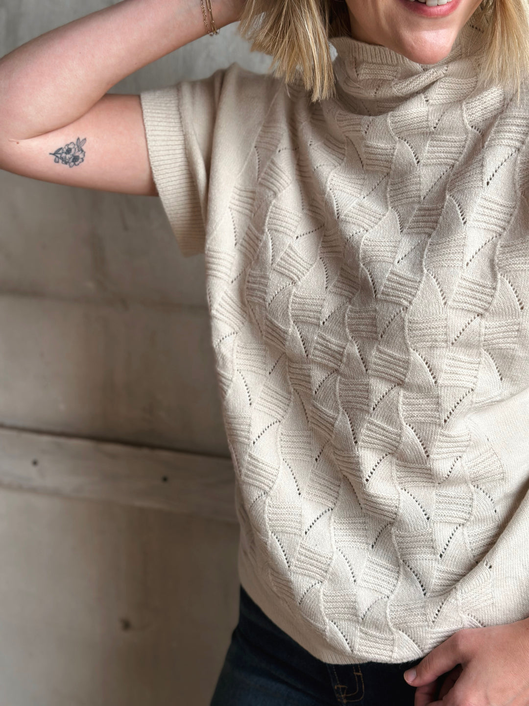 Person wearing a beige cable knit sweater with a neutral background