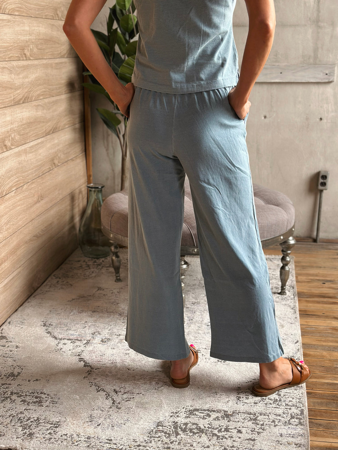 A person wearing light blue pants standing in a room with a wooden floor and gray walls.