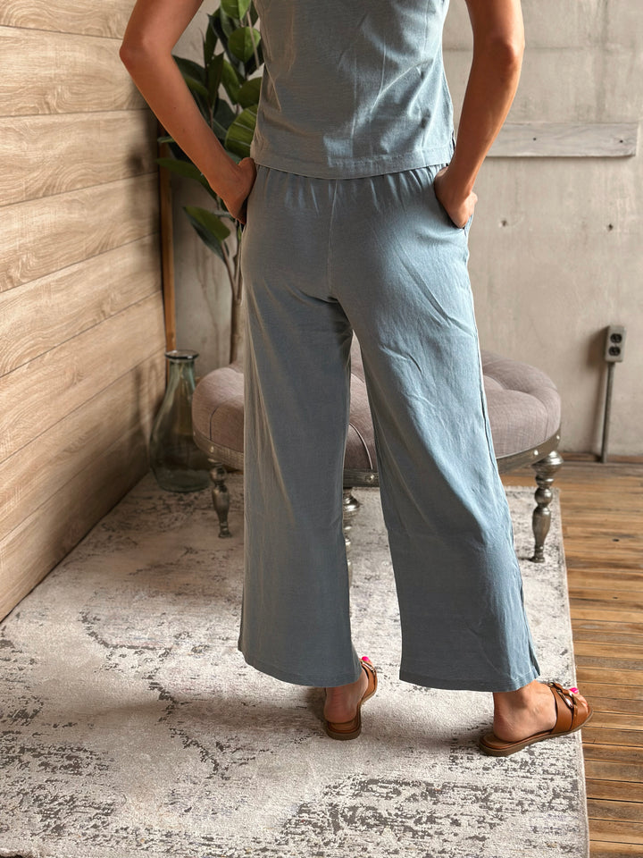 A person wearing light blue pants standing in a room with a wooden floor and gray walls.