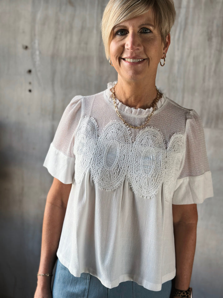 Woman wearing a white blouse with lace details against a neutral background
