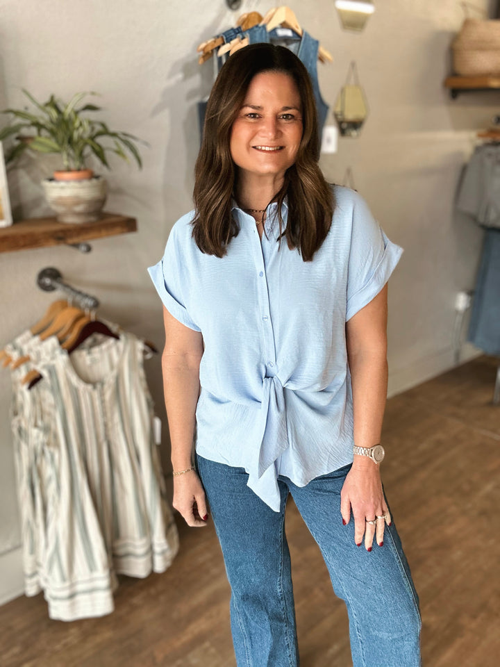 Woman wearing a light blue shirt with a tie detail in a clothing store.