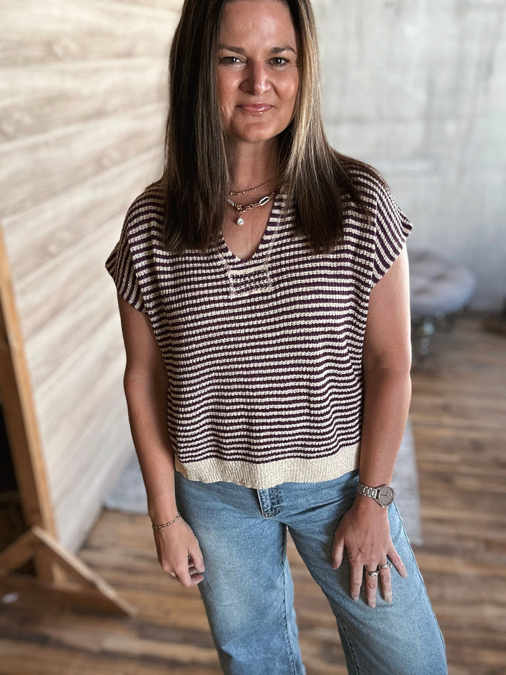 Woman wearing a beige and plum striped v-neck shirt and jeans standing indoors.