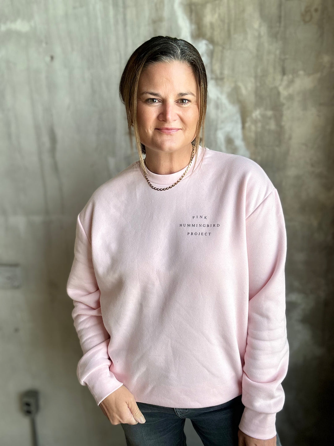 Woman wearing a light pink crewneck sweatshirt with small chest lettering