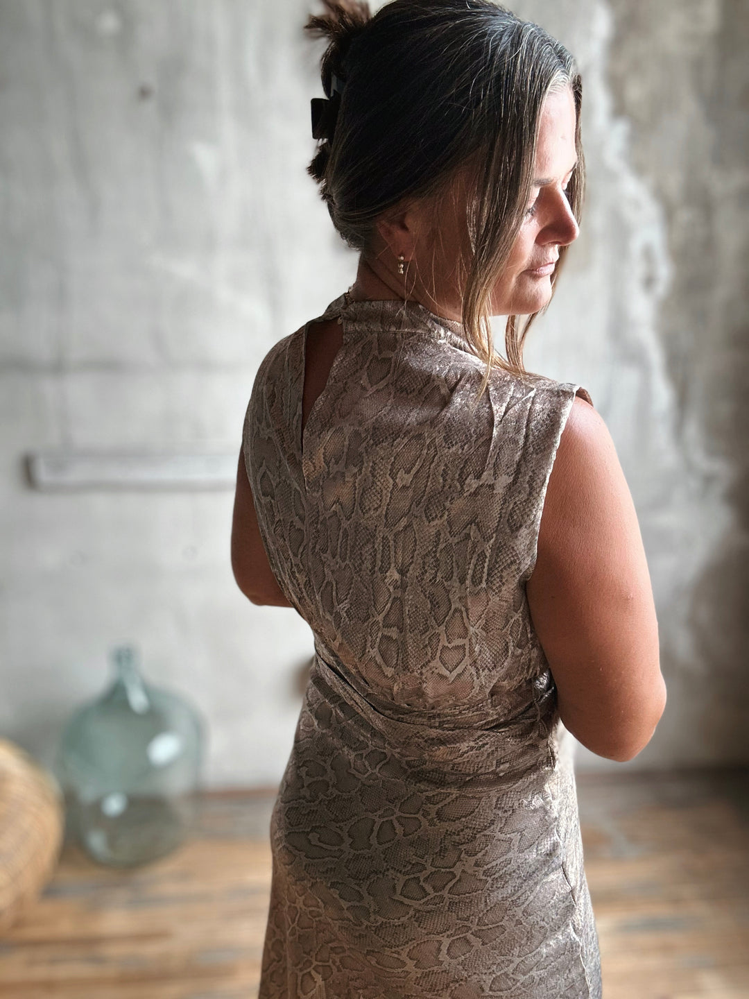 Woman wearing a patterned dress in a room with a textured wall and wooden floor.