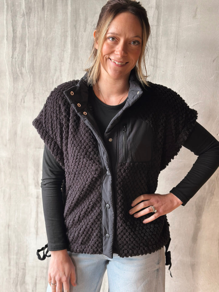 Woman wearing a black knitted vest over a dark shirt with a light background