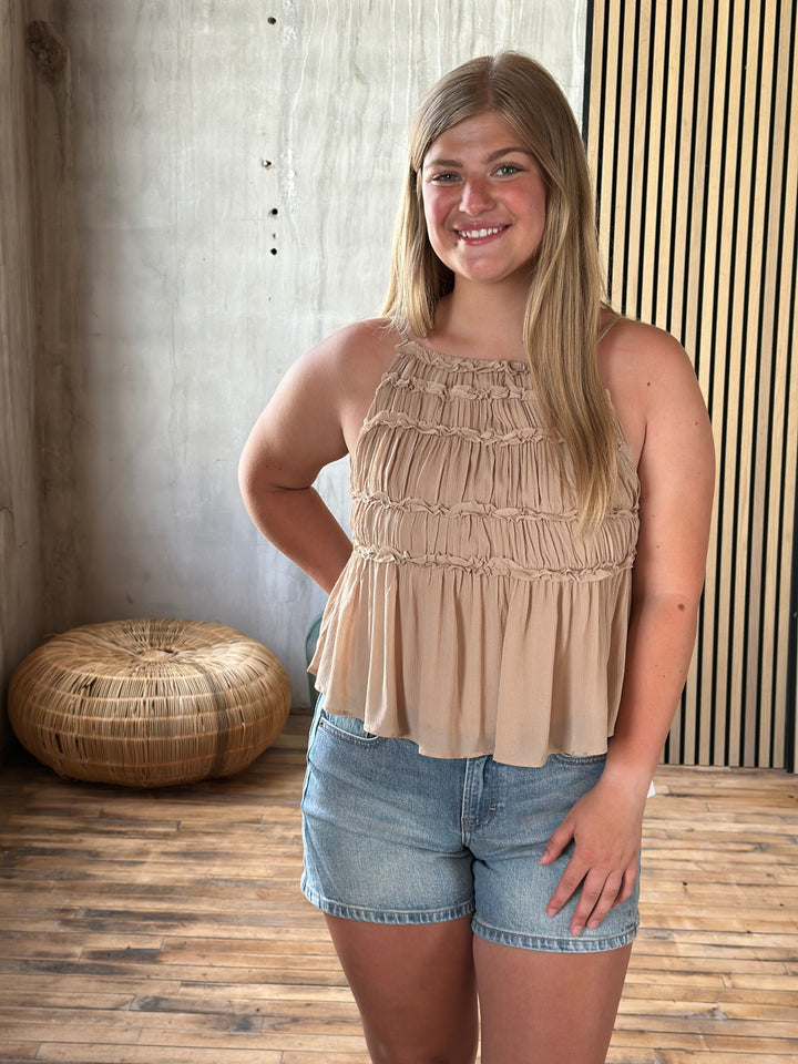 Woman in a beige top and denim shorts standing on a wooden floor.