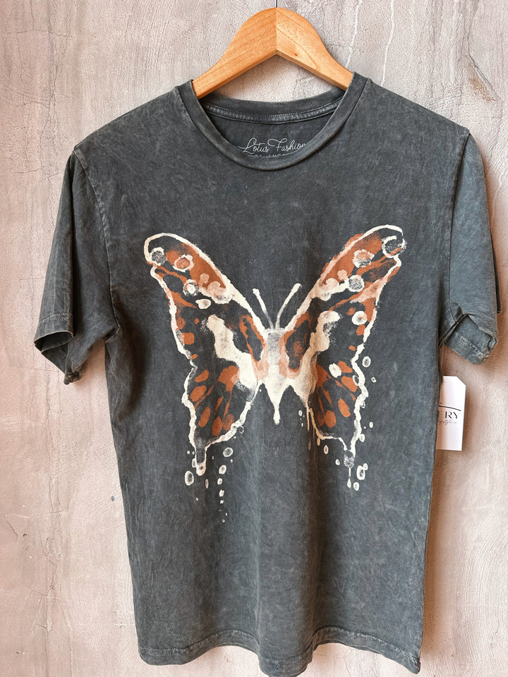 Gray t-shirt with a butterfly design on a wooden hanger against a wooden background.
