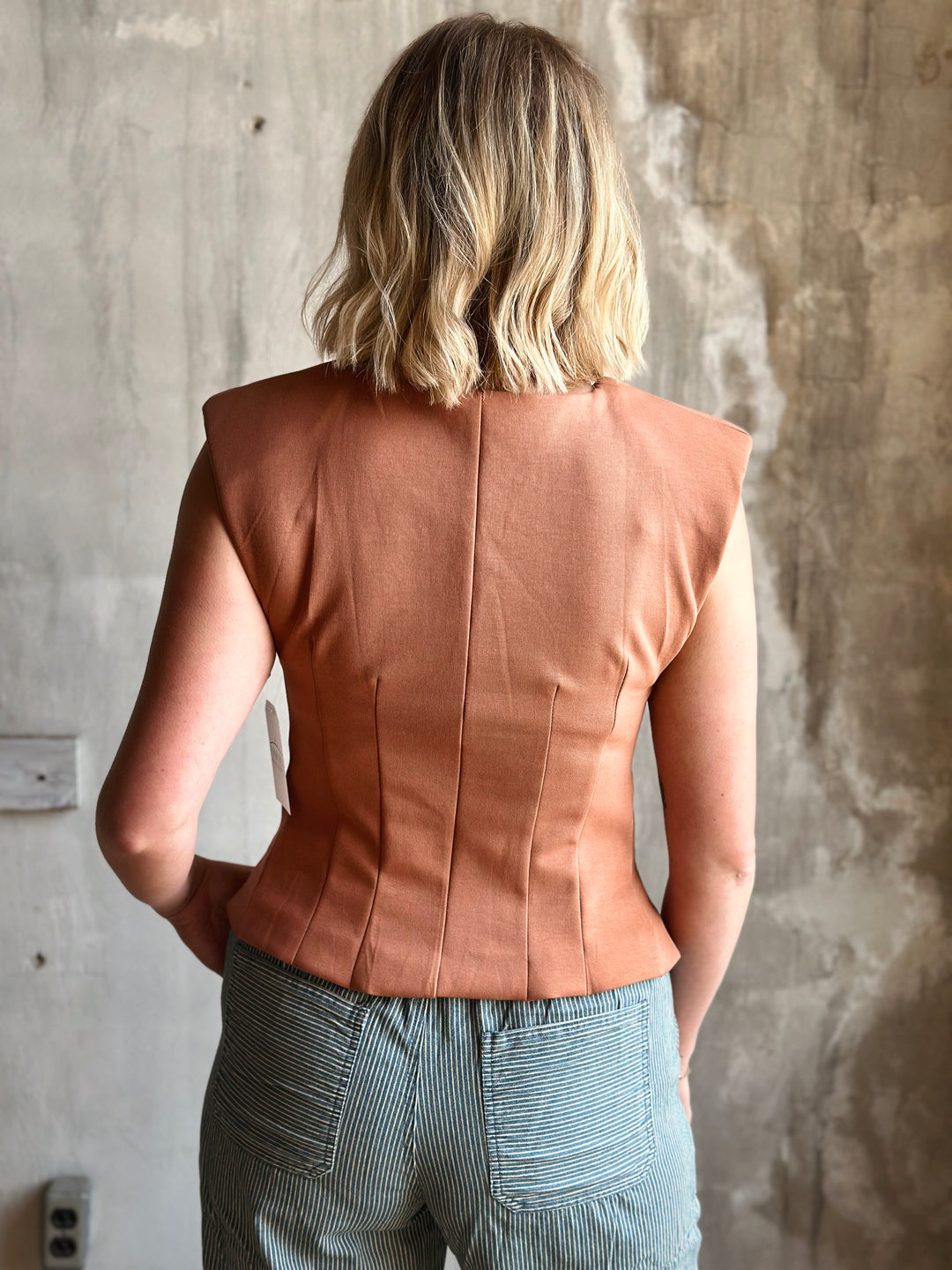Person wearing a brown leather vest against a textured wall.