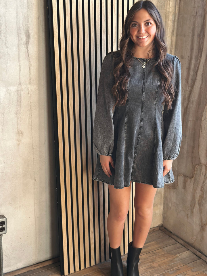 Woman wearing a denim dress standing against a textured wall.