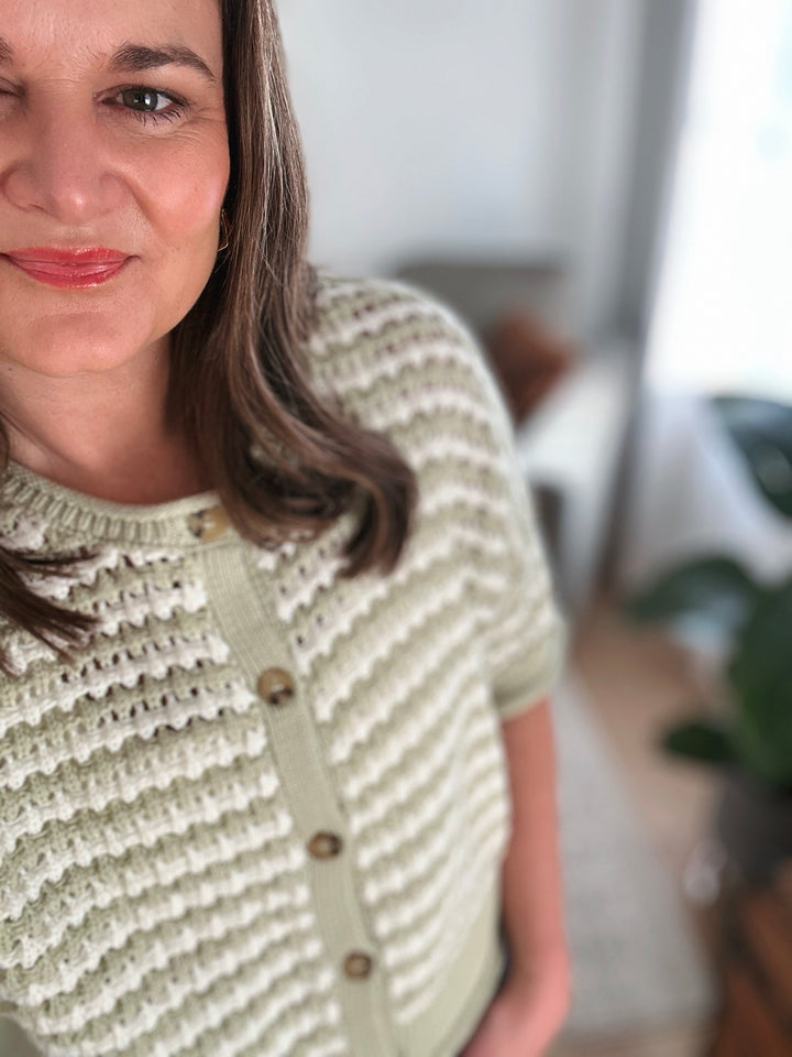 Woman wearing a green knitted cardigan with a blurred indoor background