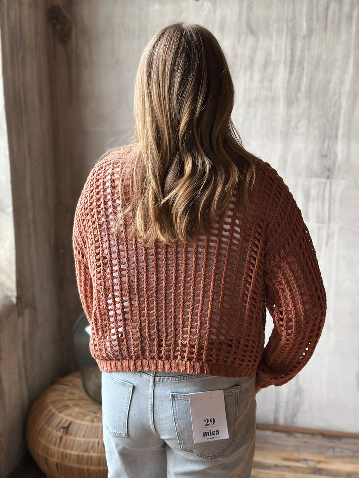 A person wearing a light brown knitted sweater, standing against a neutral background.
