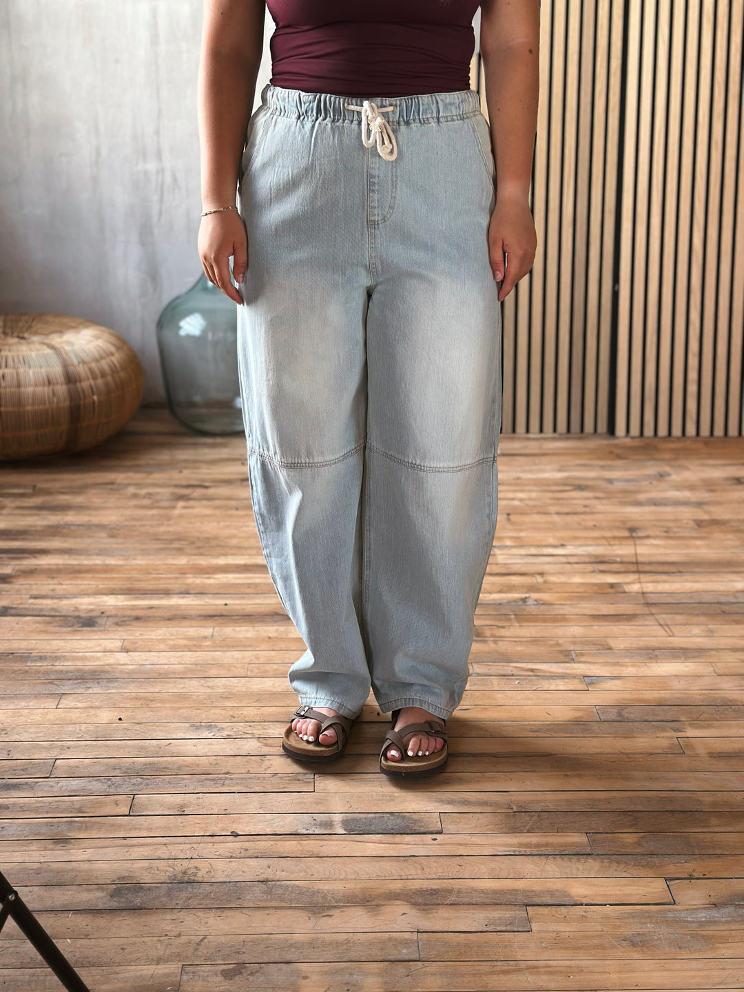 A person wearing light washed jeans standing on a wooden floor with a neutral background.
