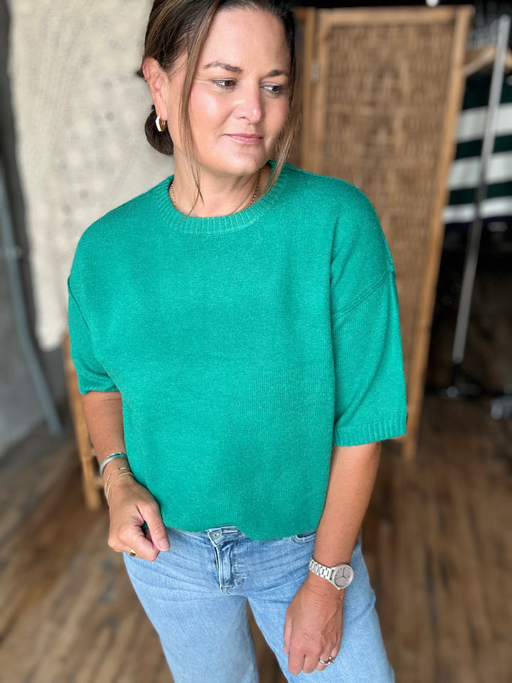 A woman wearing a bright green short-sleeve knit sweater and light blue jeans.