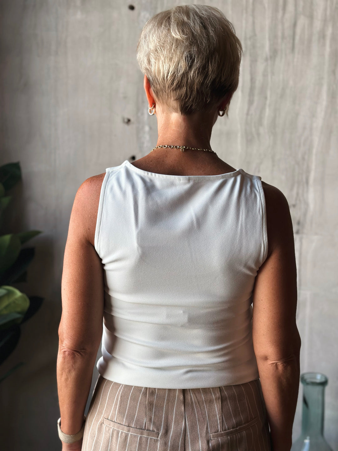Person wearing a white sleeveless top and beige pants with a neutral background