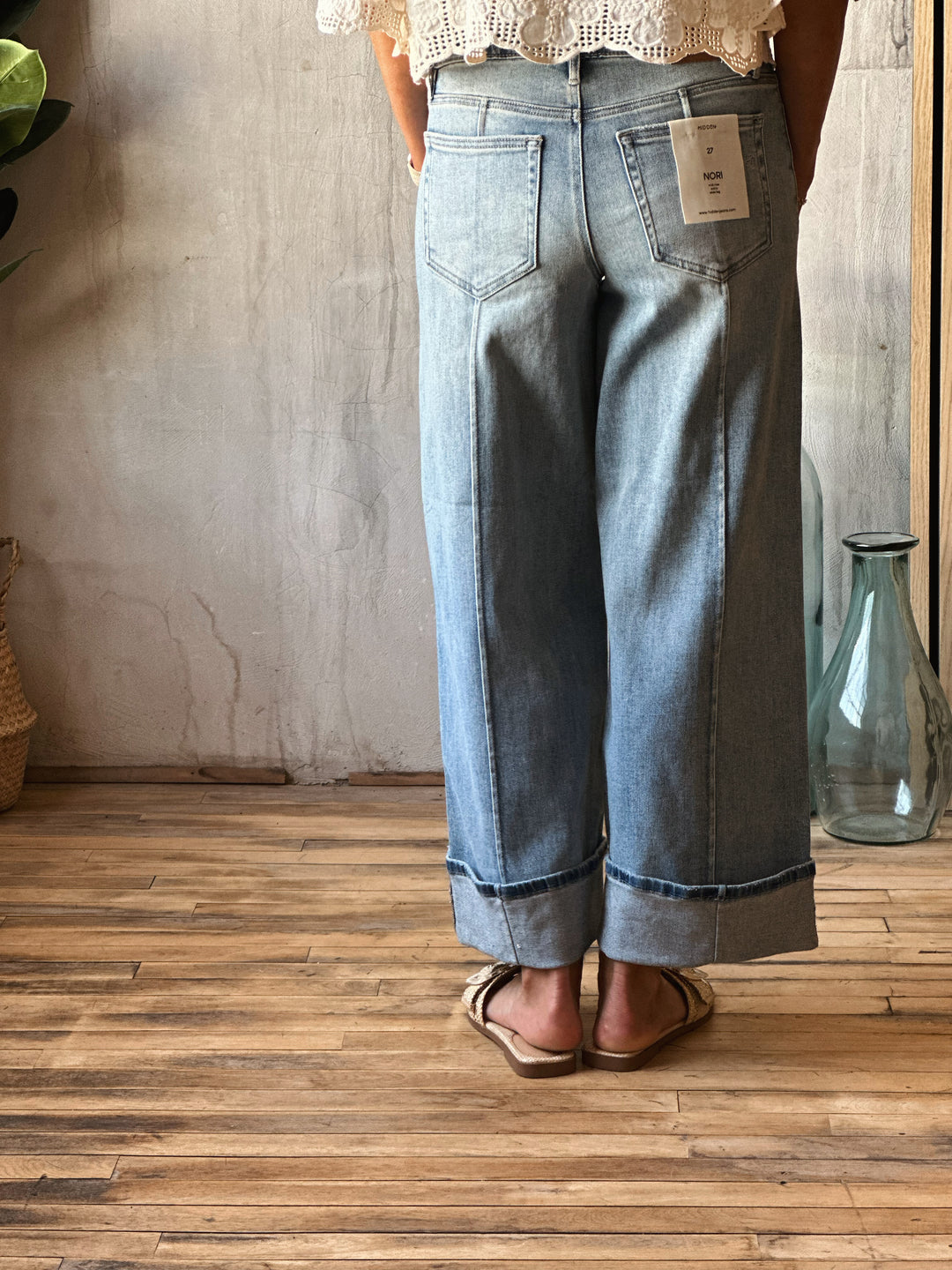 Person wearing light blue jeans with a tag, standing on a wooden floor.