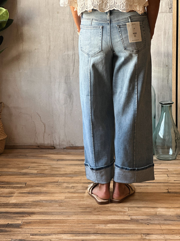 Person wearing light blue jeans with a tag, standing on a wooden floor.