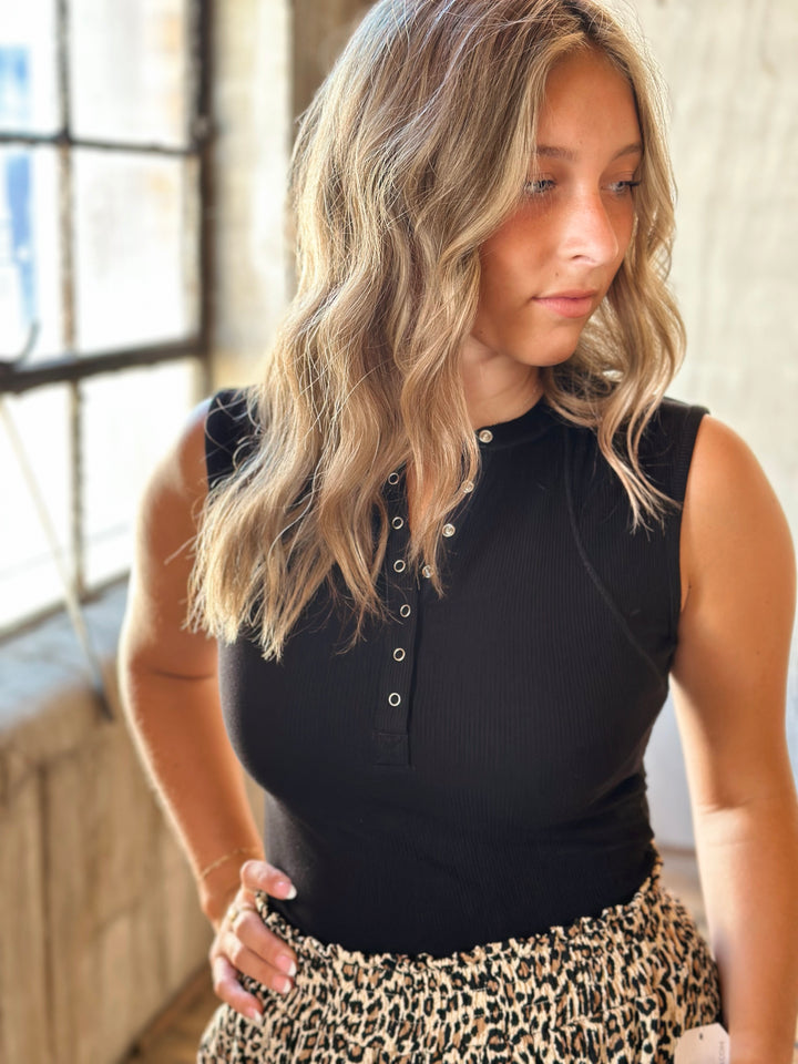 Woman wearing a black sleeveless top and leopard print pants indoors.