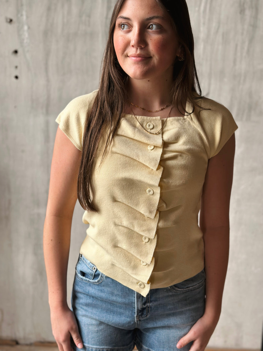 Woman wearing a beige top with button details against a wooden background