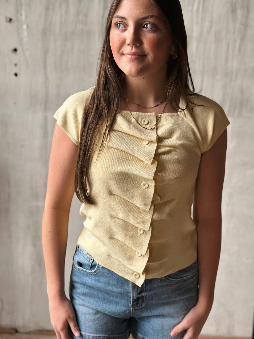 Woman wearing a beige top with button details against a wooden background