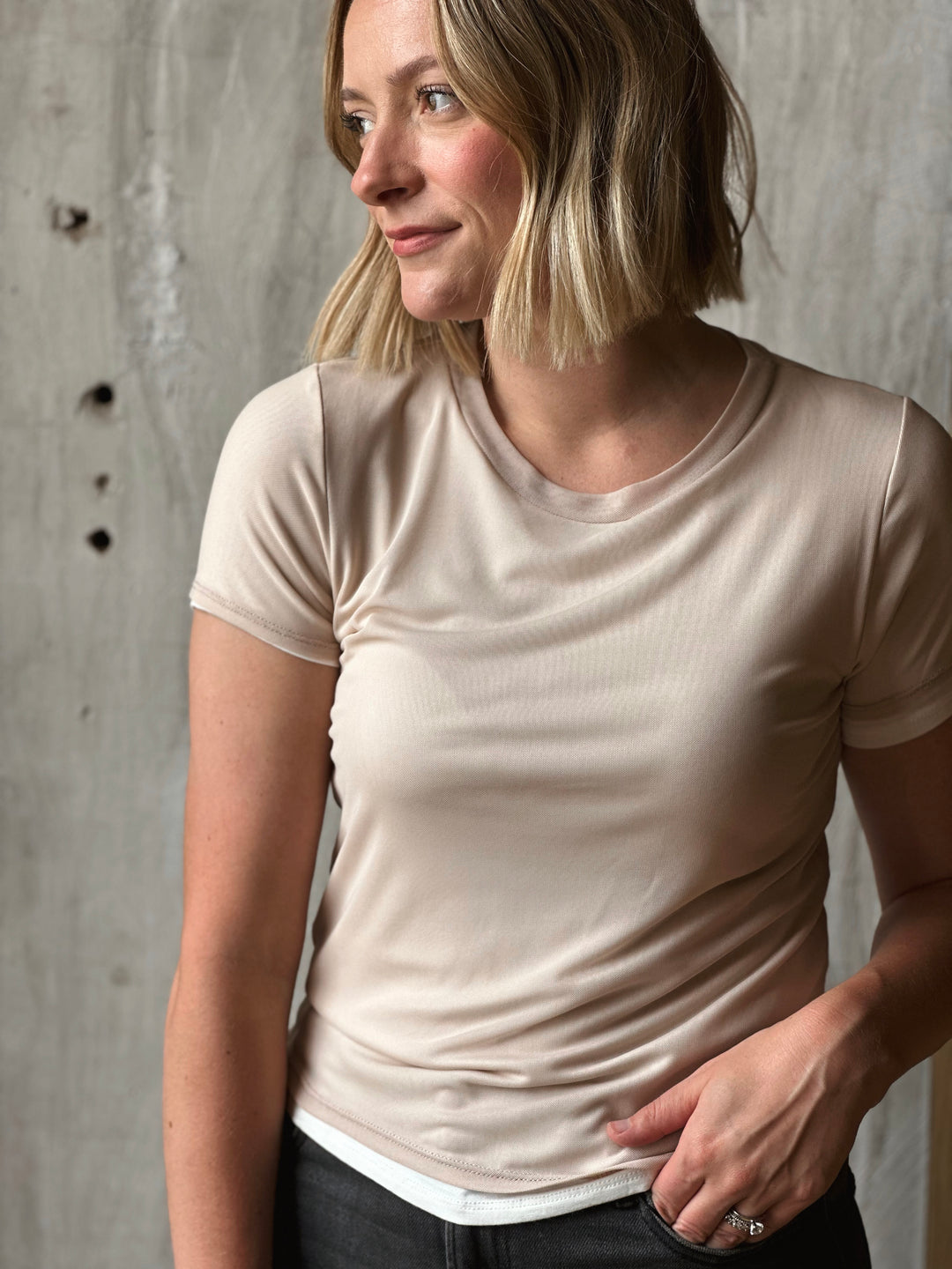 Woman wearing a beige t-shirt against a concrete wall