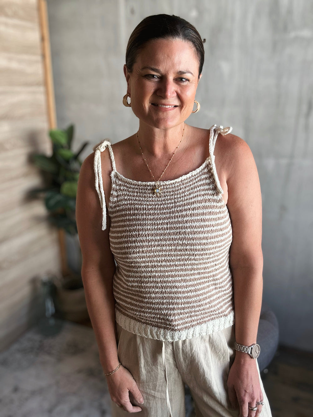 A woman wearing a light brown and beige striped crocheted tank top with thin straps that are tied into small bows.