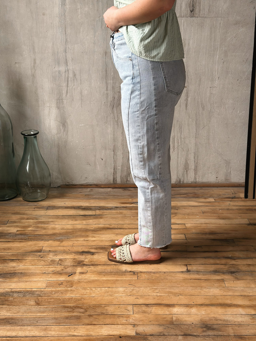 Person wearing light blue jeans standing on a wooden floor with a gray wall background