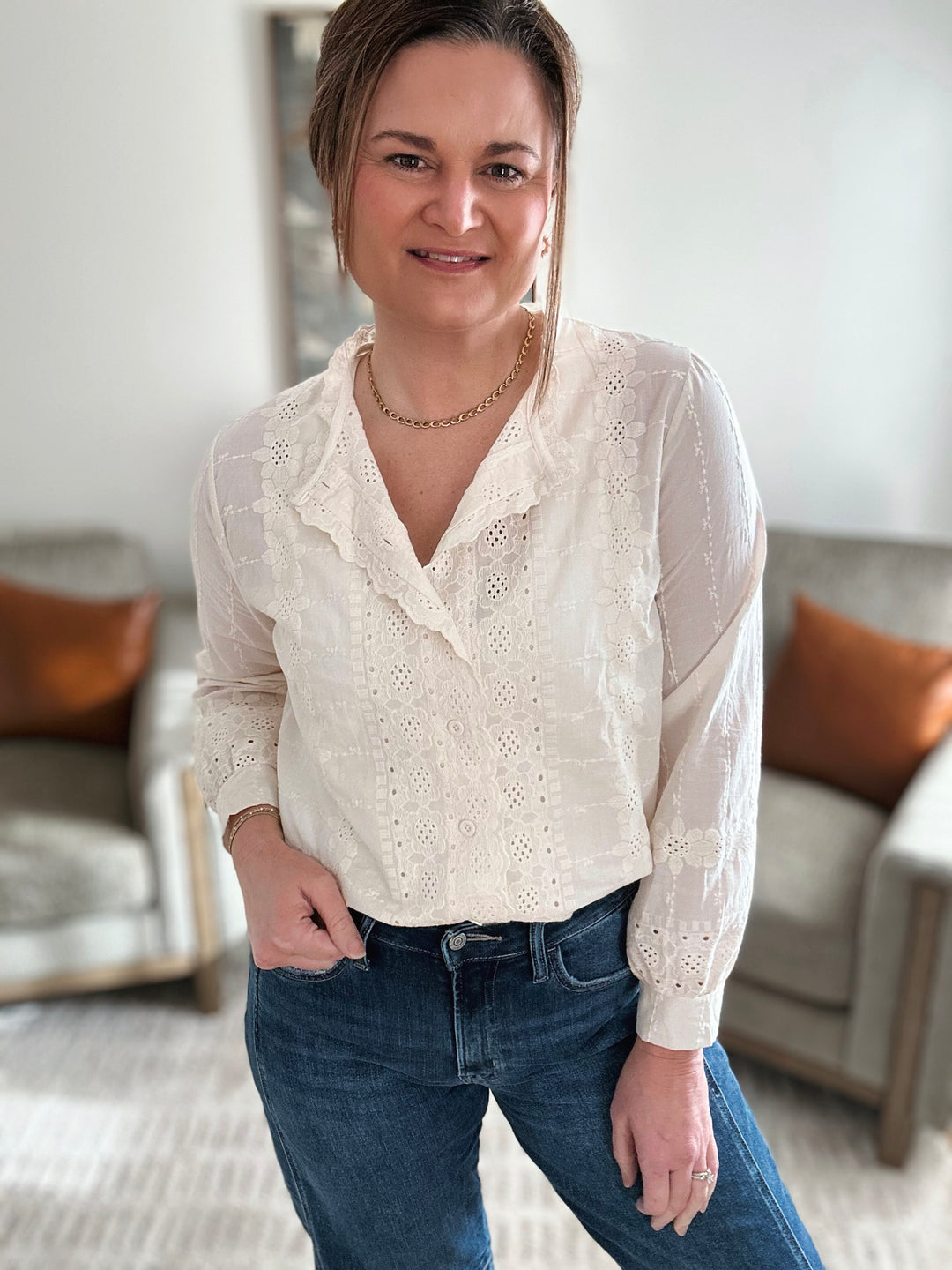 Woman wearing a white blouse with lace details and blue jeans in a living room setting.