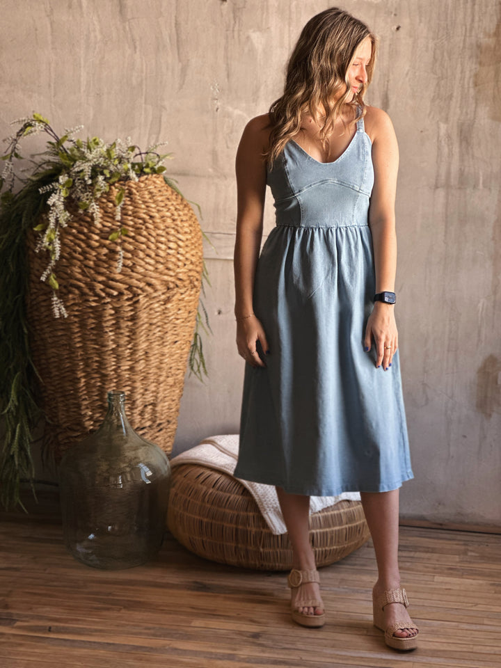 Front view of model wearing a flare dress that has a stretch denim fit with a sweetheart neckline, wide straps, and it is a light Denim color 