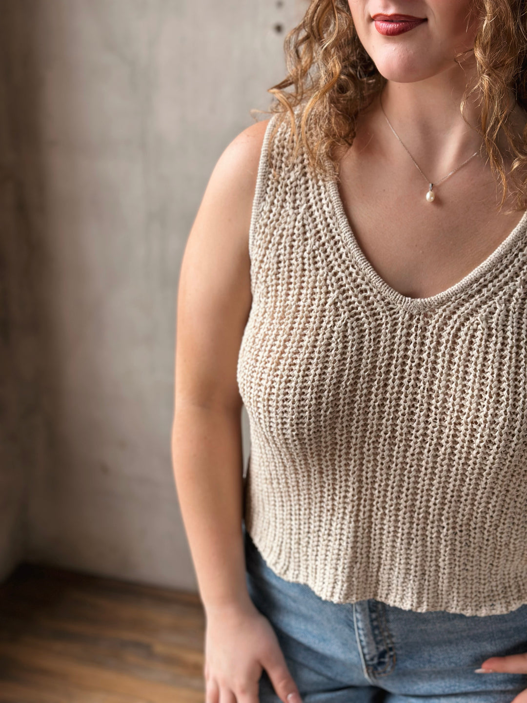 Woman wearing a beige knitted tank top against a neutral background