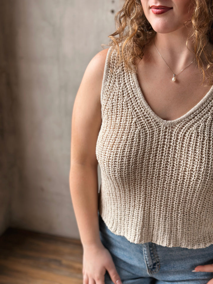Woman wearing a beige knitted tank top against a neutral background